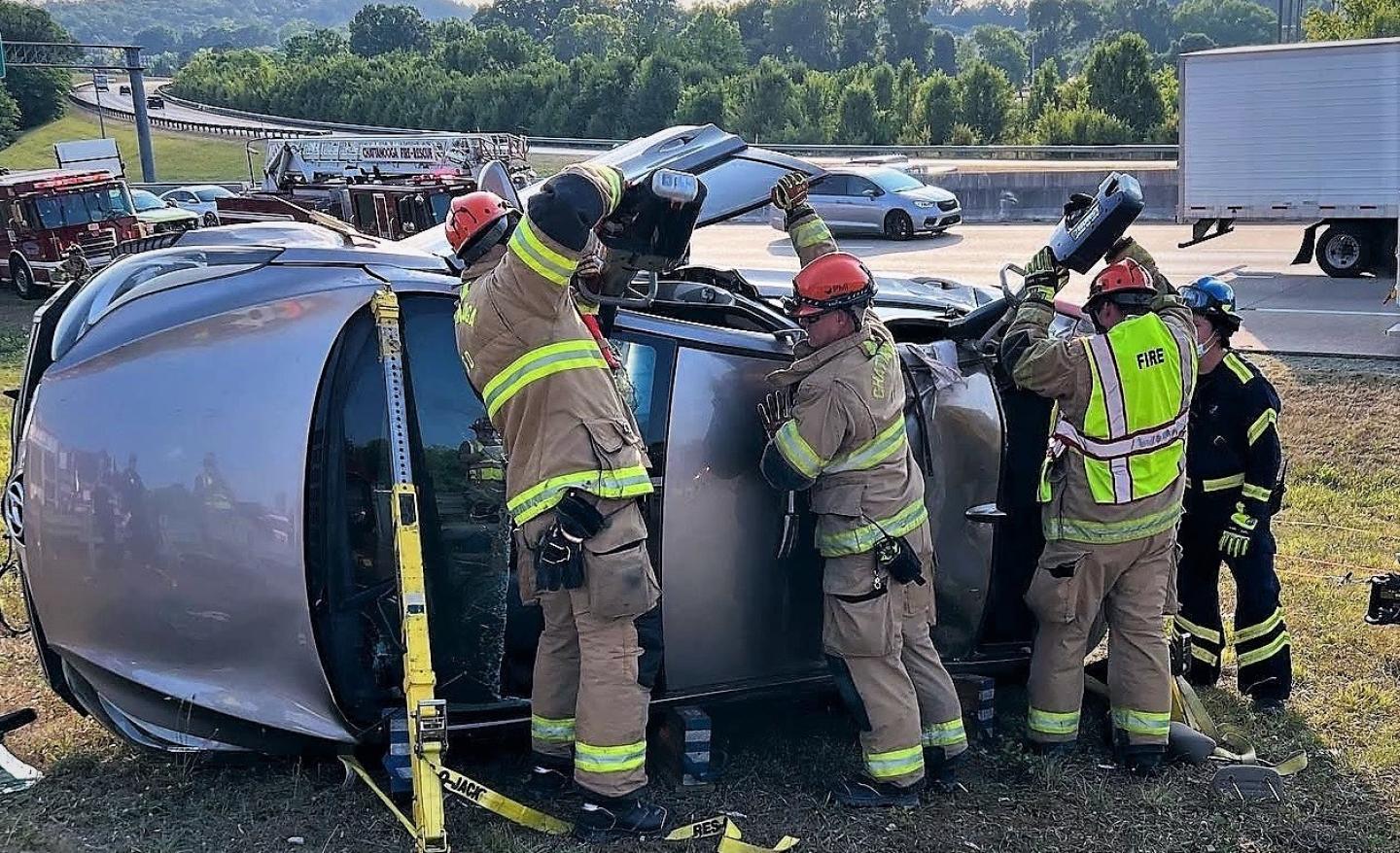 A car flipped on its side in the road, with the fire department performing an extrication.