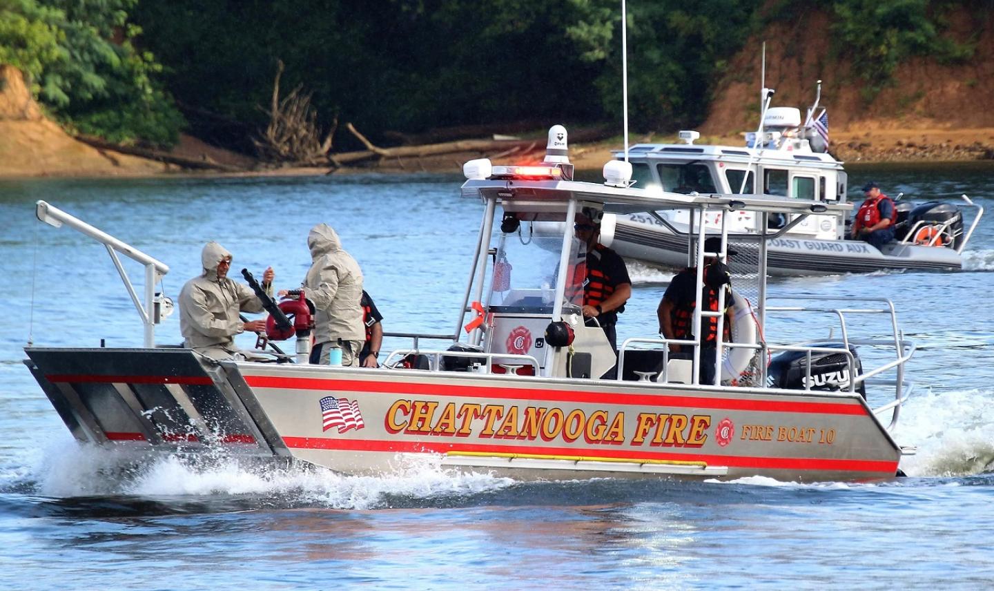 People on a boat in the water, with fire department visible in the background.