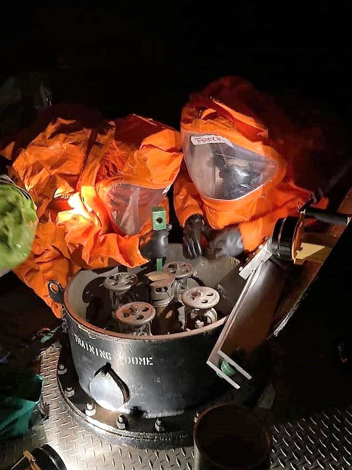  A table with two individuals wearing orange suits, amidst various objects.