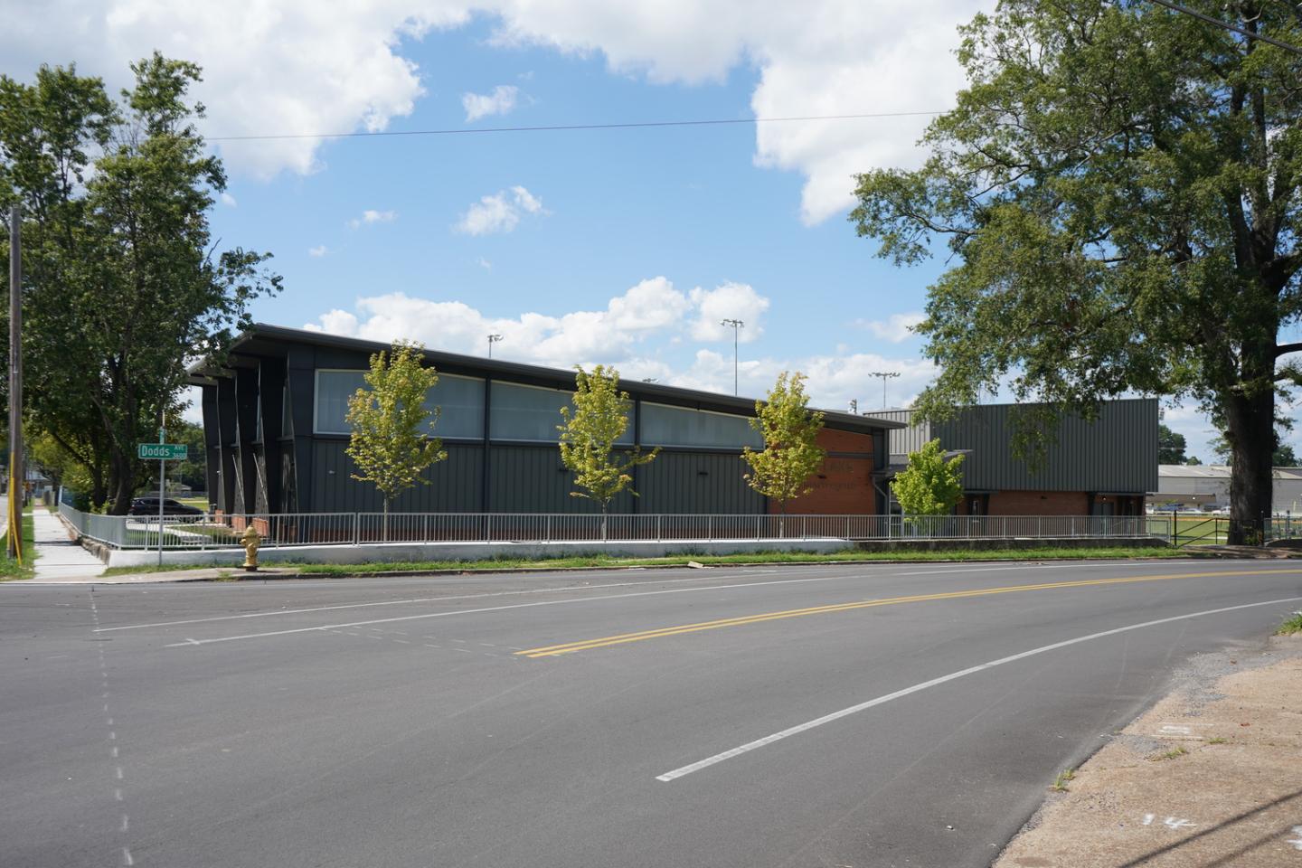 Modern grey and red brick building of East Lake Community Center with large glass windows, surrounded by green trees and a clear blue sky with scattered clouds