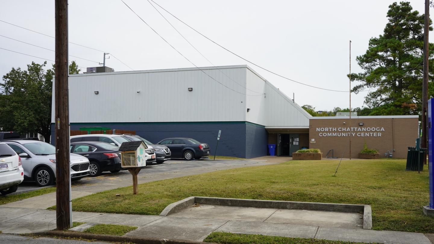 North Chattanooga Community Center exterior with white and dark blue walls, beige sign, parked cars, and a large tre