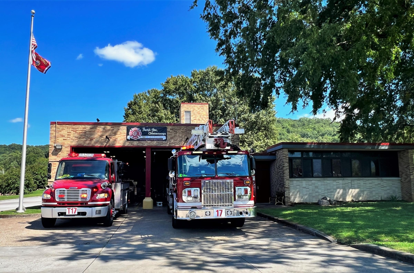 Two fire trucks parked in front of a building next to a pole with an american flag waving at fire station 17