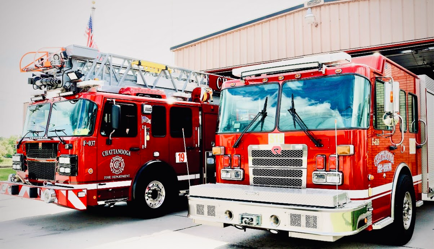 Side view of two red fire trucks parked in front of a building at fire station 19.