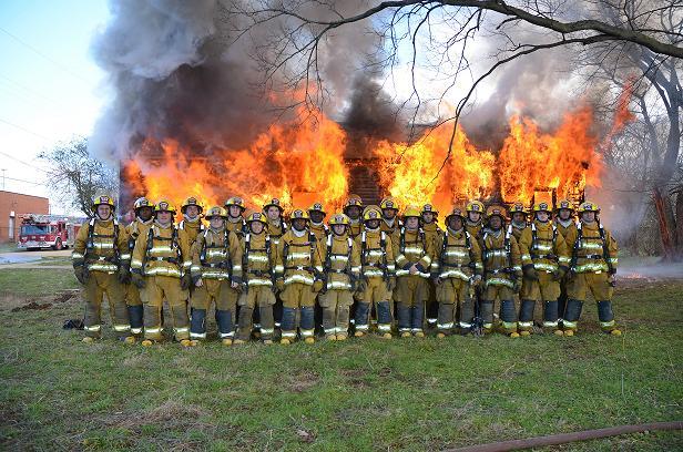 A group of firefighters posing in front of a burning house, bravely battling the flames.