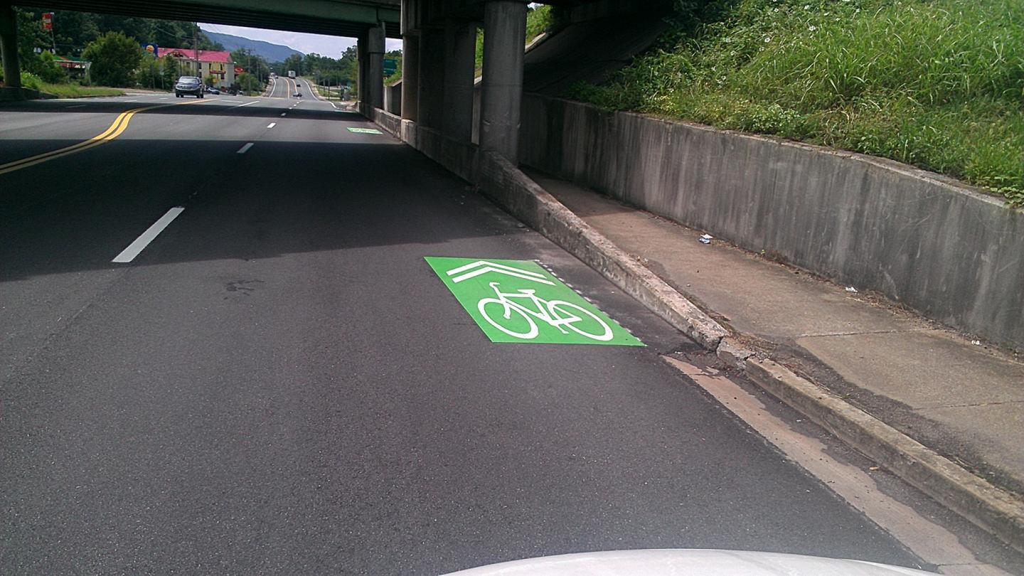 A white car driving on a road with a shared bike lane.