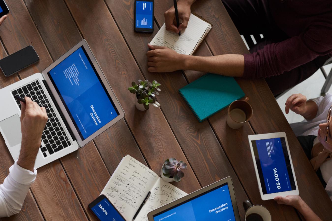 Group of people with devices around wooden desk